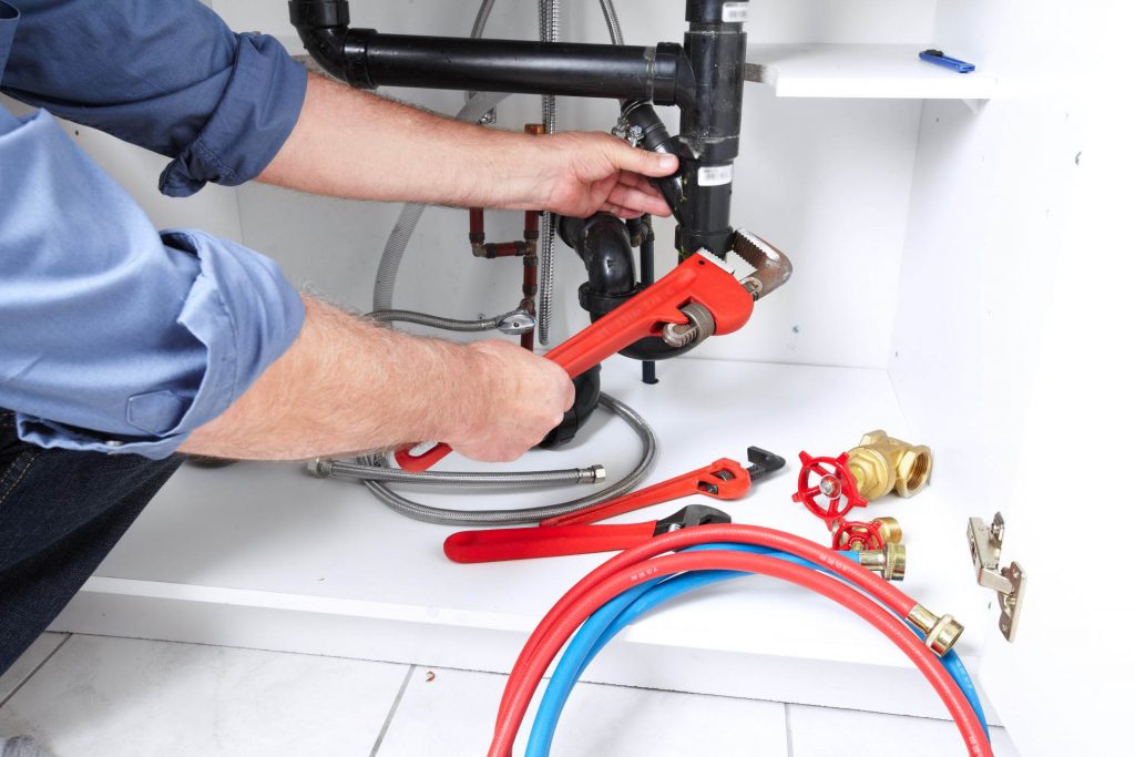 Hands of professional Plumber with a wrench. Clogged sink.