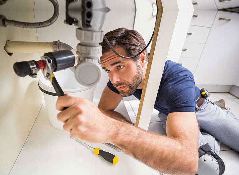 Plumber working under the kitchen sink with tools.