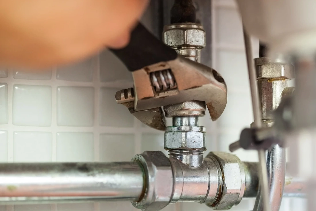 Plumber tightening a pipe fitting with wrench.