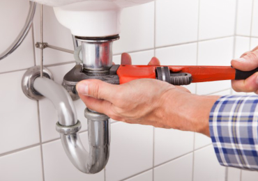 Tightening a pipe under the sink with wrench.