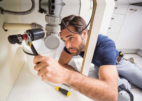 blog2.jpg Plumber working under the kitchen sink with tools.
